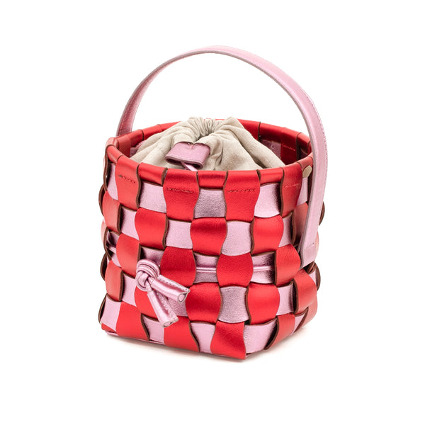 Bolsa bucket em couro trançado vermelho e rosa, estruturada com alça curta e fecho de cordão regulável. Estilo artesanal contemporâneo.