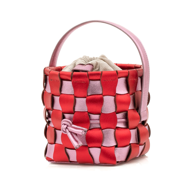 Bolsa bucket estruturada em couro vermelho e rosa trançado, com alça curta e fecho ajustável em cordão. Design moderno e artesanal.