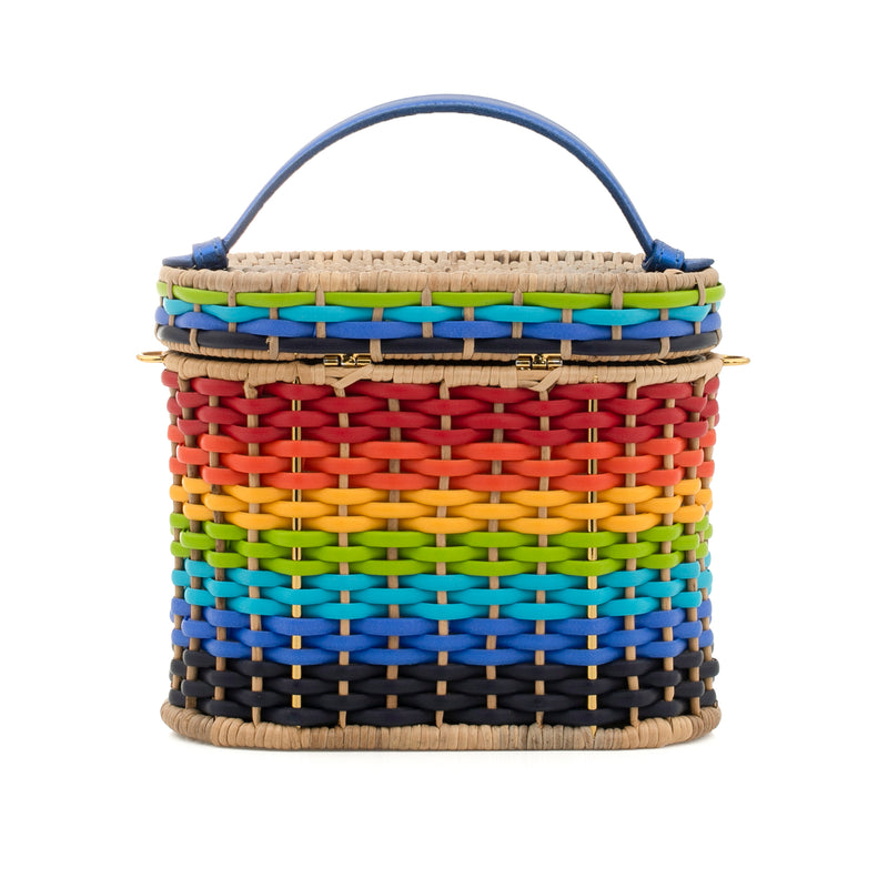 Bolsa artesanal em palha estruturada, com trama multicolorida em degradê, fecho redondo em couro laranja com símbolo solar e alça curta em couro azul.