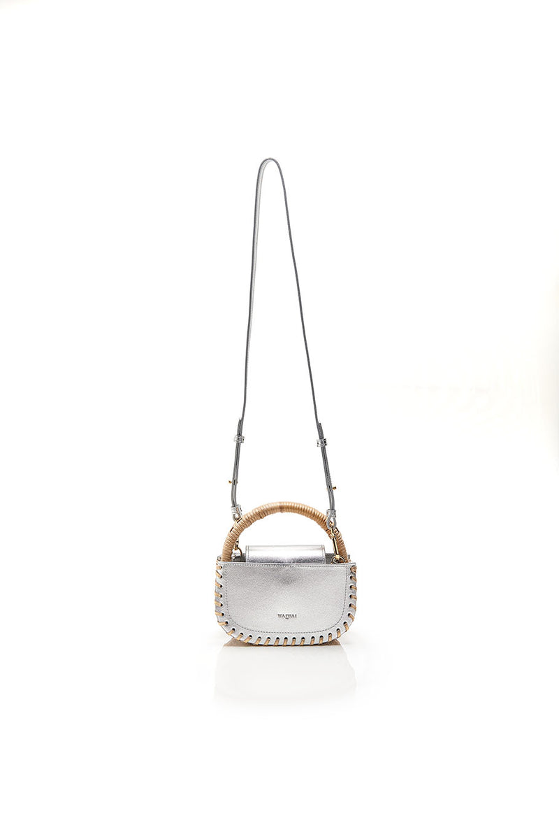Bolsa de couro prateado com detalhes de costura nas bordas e alça estruturada em rattan natural.