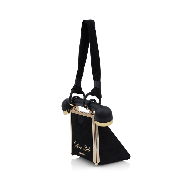 Bolsa estruturada preta inspirada em telefone retrô, com detalhe de disco dourado na frente e alça que lembra o fone.