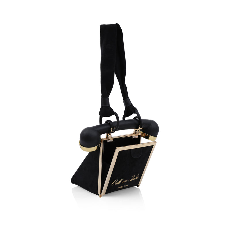 Bolsa preta estruturada em formato de telefone retrô, disco dourado na frente e alça superior inspirada no fone.