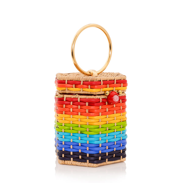 Bolsa estruturada em rattan com trama em degradê de cores do arco-íris, fecho esférico vermelho e alça metálica circular dourada.