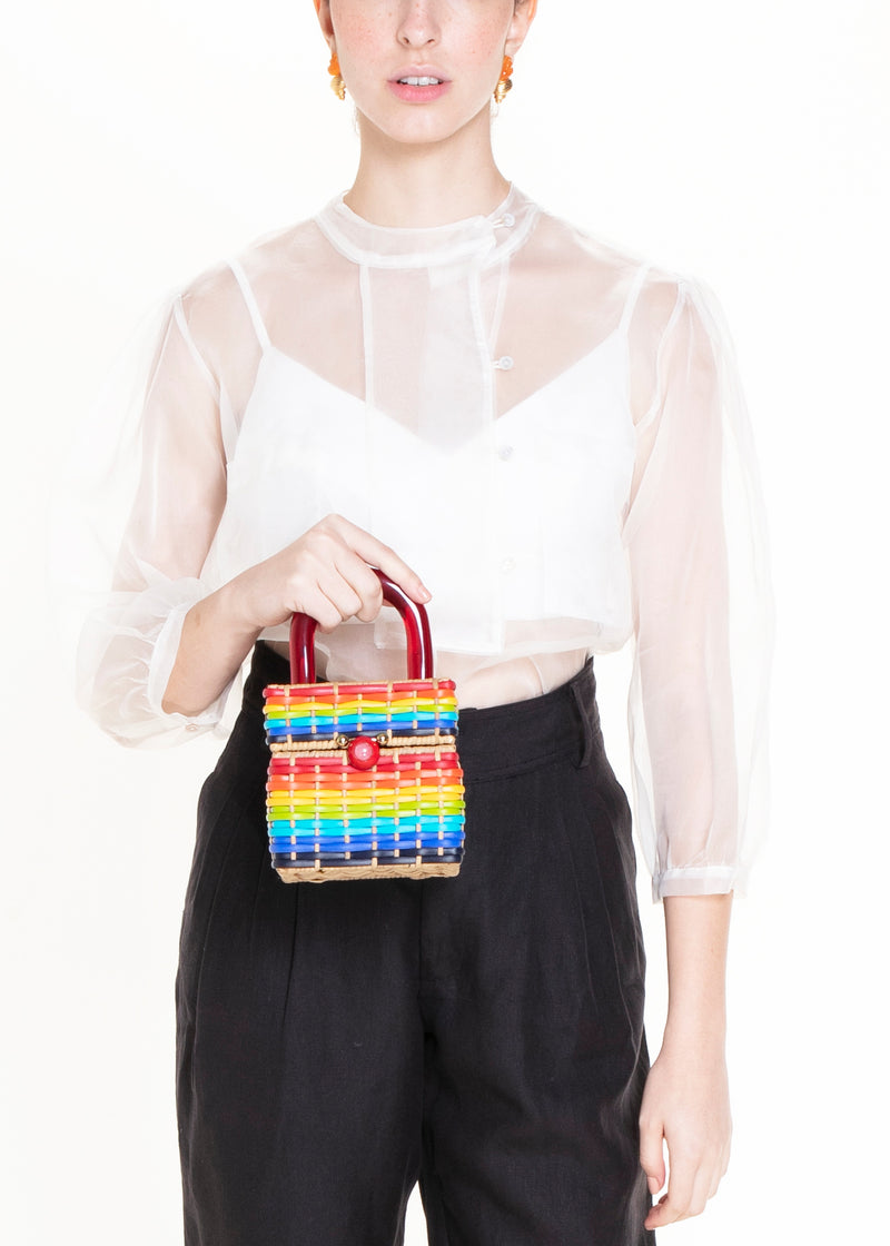 Bolsa estruturada em rattan com trama em cores do arco-íris, alça rígida em acrílico vermelho e fecho esférico vermelho central.