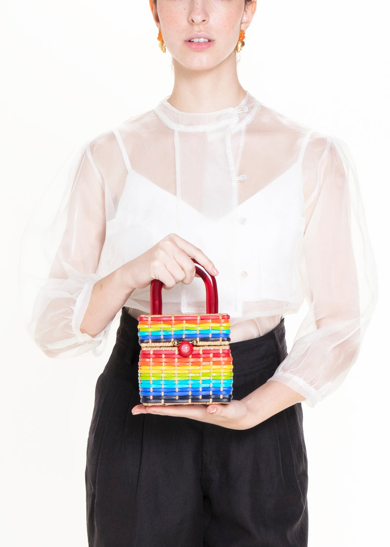 Bolsa estruturada em rattan com trama em cores do arco-íris, alça rígida em acrílico vermelho e fecho esférico vermelho central.