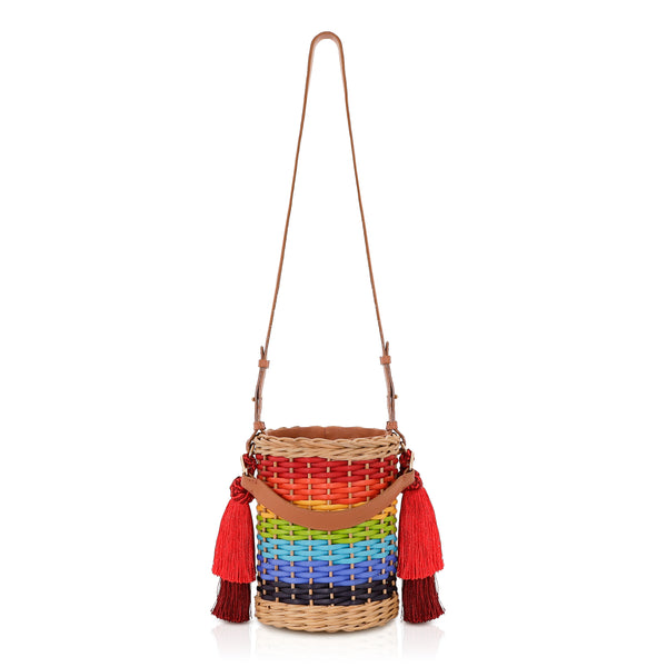 Bolsa estruturada em rattan com trama em degradê de cores do arco-íris, alça longa em couro marrom e tassels vermelhos laterais.