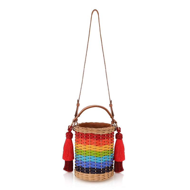 Bolsa estruturada em rattan com trama em degradê de cores do arco-íris, alça longa em couro marrom e tassels vermelhos laterais.
