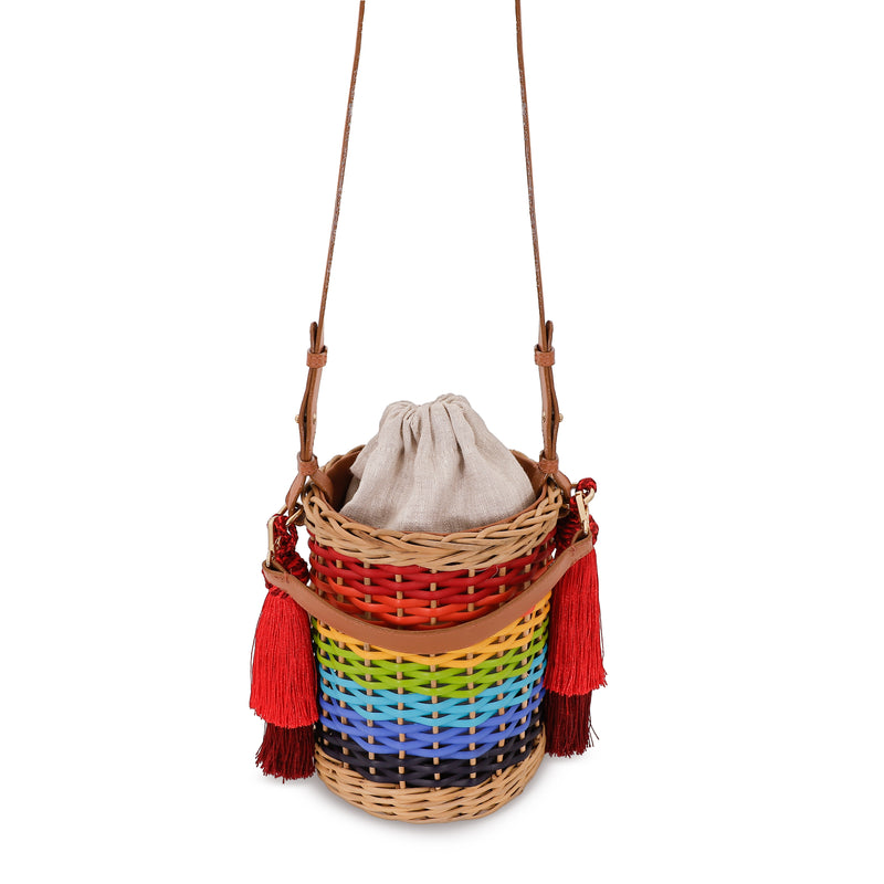 Bolsa estruturada em rattan com trama em degradê de cores do arco-íris, alça longa em couro marrom e tassels vermelhos laterais.