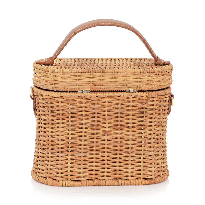 Bolsa de rattan natural com alça curta em couro bege e fecho circular em couro com detalhe em formato de raio de sol dourado.