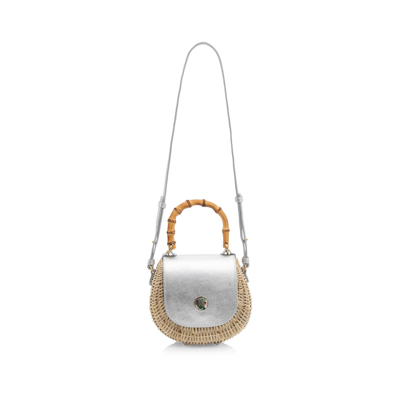 Bolsa estruturada em rattan natural, tampa em couro prateado metálico, fecho redondo em madrepérola e alça superior de bambu curvado.