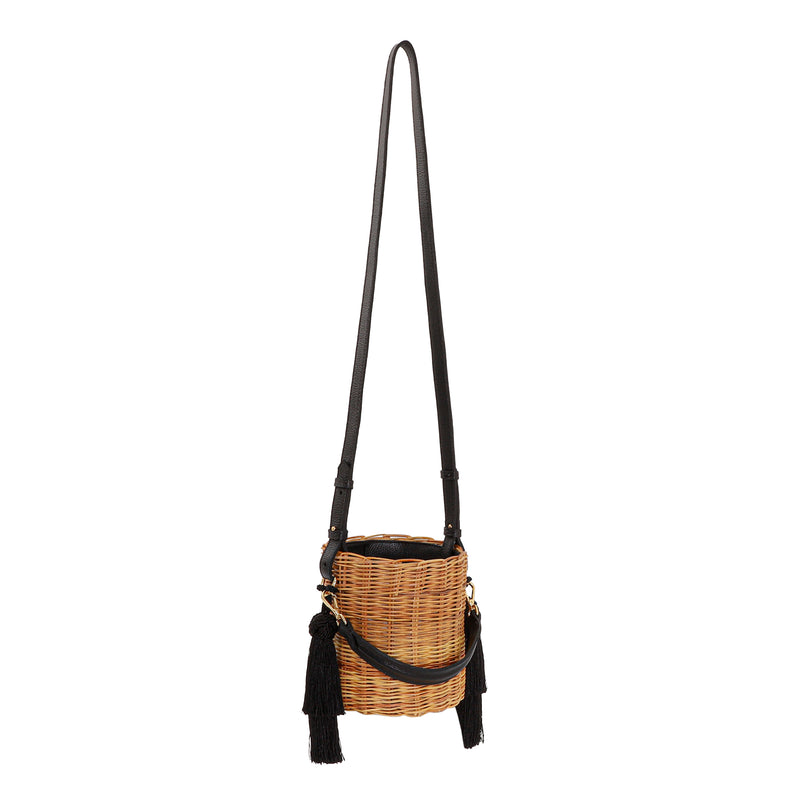 Bolsa tiracolo estruturada em rattan natural com alça longa em couro preto e detalhes em tassels pretos laterais.