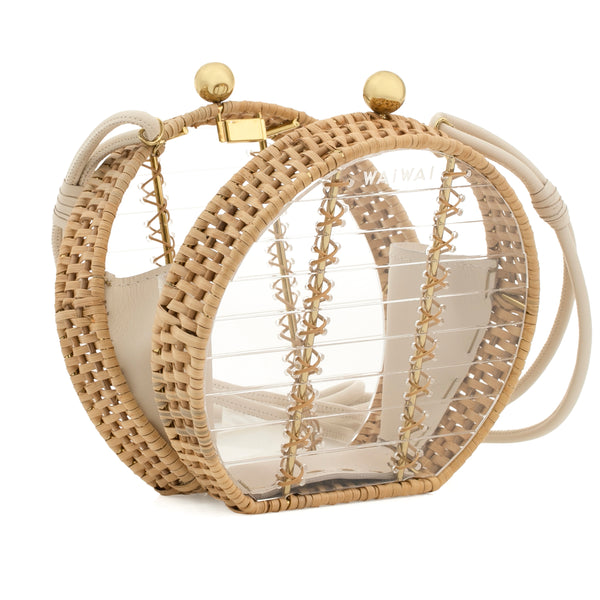 Bolsa redonda estruturada em acrílico transparente, com bordas em rattan natural, alça tiracolo removível em couro bege, fecho esférico dourado e interior compartimentado em couro bege.