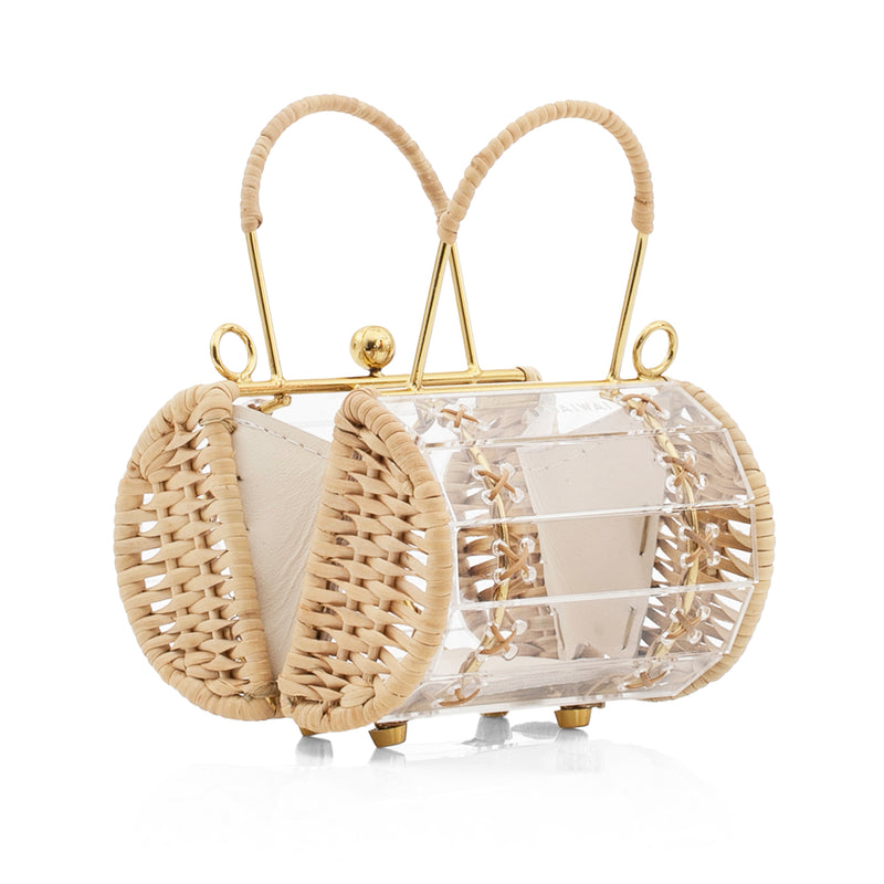 Bolsa estruturada em design transparente de acrílico, detalhes dourados, laterais em couro bege e alça curta de palha.