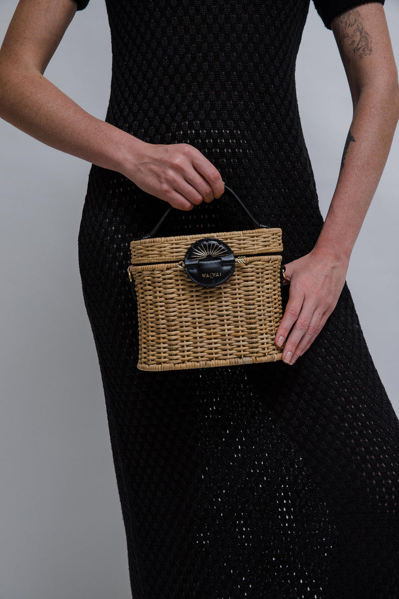 Bolsa estruturada em vime natural com alça curta em couro preto e fecho redondo em couro com detalhe em baixo-relevo dourado em formato de sol nascente.