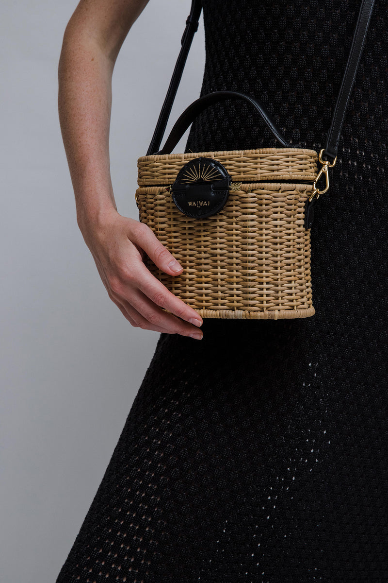 Bolsa estruturada em vime natural com alça curta em couro preto e fecho redondo em couro com detalhe em baixo-relevo dourado em formato de sol nascente.