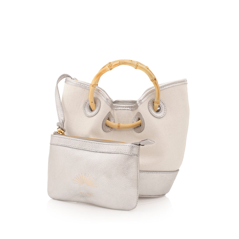 Bolsa bucket estruturada em canvas cru com couro prata nos acabamentos, alça de bambu curvado e reforço em couro na base.