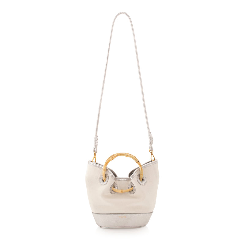 Bolsa bucket em canvas cru com detalhes prateados em couro, alça curta de bambu curvado e acabamento superior e inferior em couro.