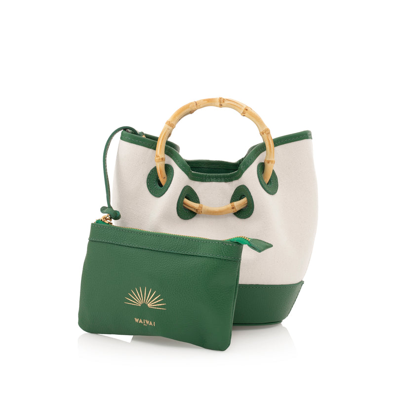 Bolsa bucket em canvas bege, detalhes em couro verde e alça estruturada em bambu natural. Estilo atemporal com toque tropical.