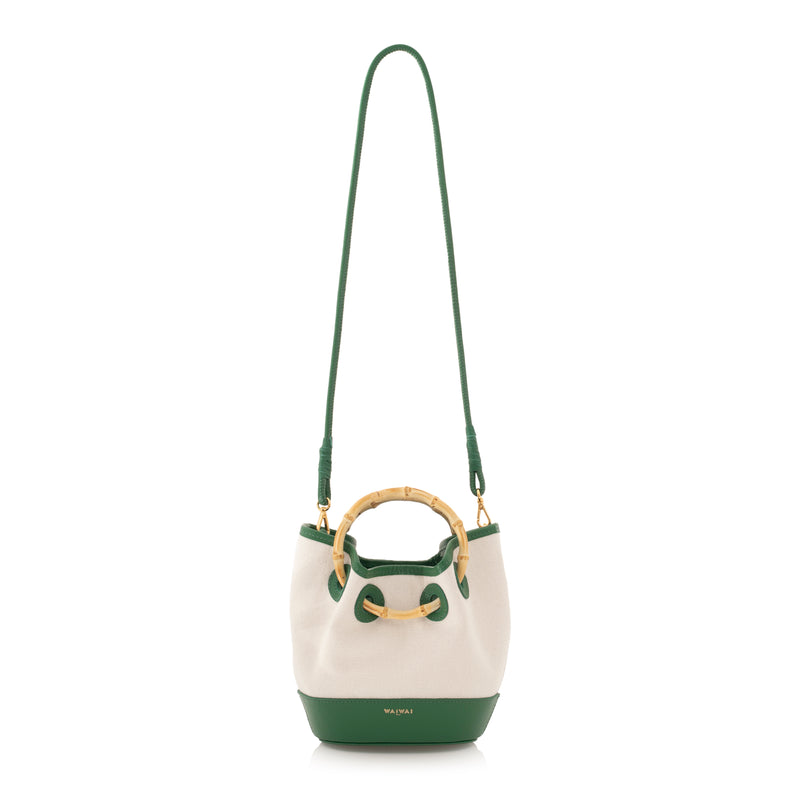 Bolsa bucket estruturada em canvas bege com couro verde nos acabamentos e alça de bambu natural.