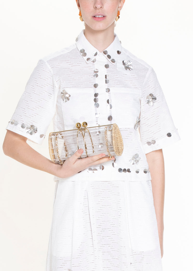 Clutch retangular em acrílico transparente com laterais em rattan, detalhe de costura em X e fecho esférico dourado.