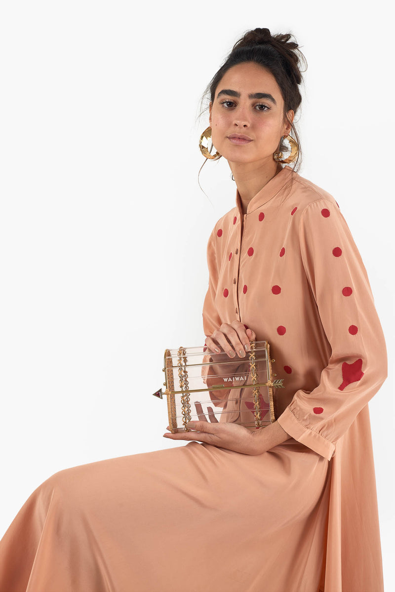 Clutch em acrílico transparente com laterais em rattan, detalhe de costura em X dourado e fecho em formato de flecha metálica dourada com ponta vermelha.