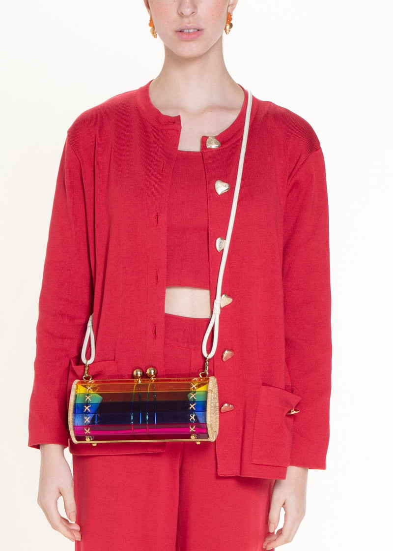 Clutch estruturada em acrílico arco-íris translúcido, listras horizontais em cores vibrantes, laterais em rattan natural e fecho esférico dourado.