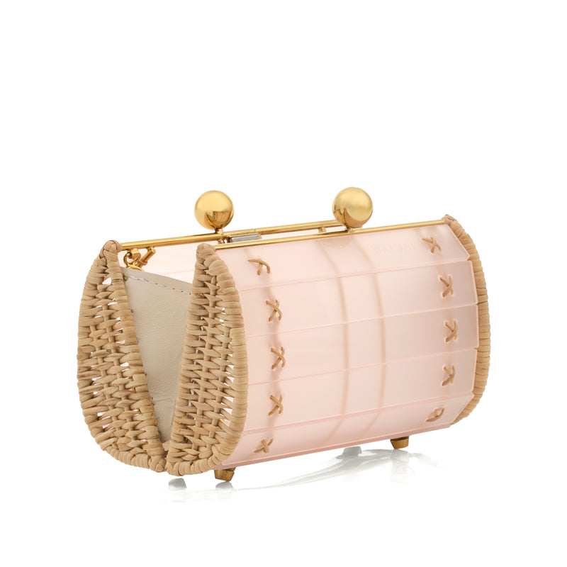 Bolsa clutch acrílica em rosa fosco, estruturada com laterais de rattan natural, ferragens douradas e fecho esférico duplo.