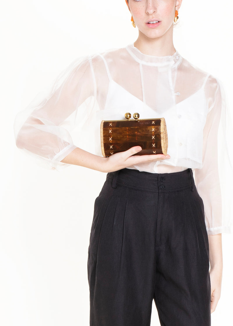 Bolsa clutch acrílica em efeito tartaruga marrom, estruturada com laterais em rattan natural, fecho esférico dourado e ferragens metálicas.